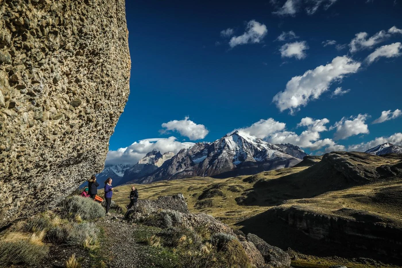 Awasi Patagonia guests and their private guide beneath a conglomerate rock overhang with the Paine massif behind
