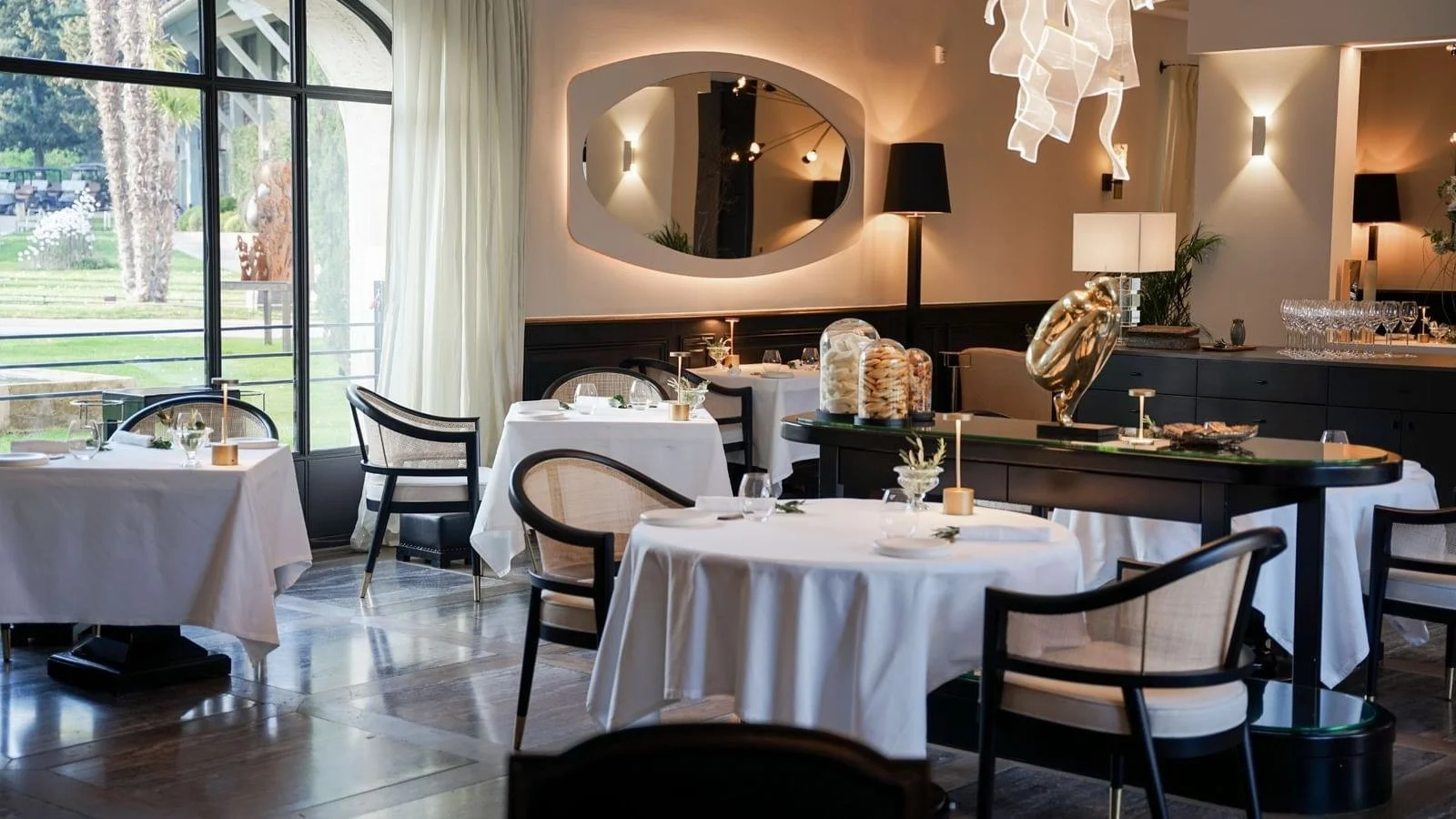 L'Aupiho restaurant dining room at Domaine de Manville with white linen tables and arched windows.