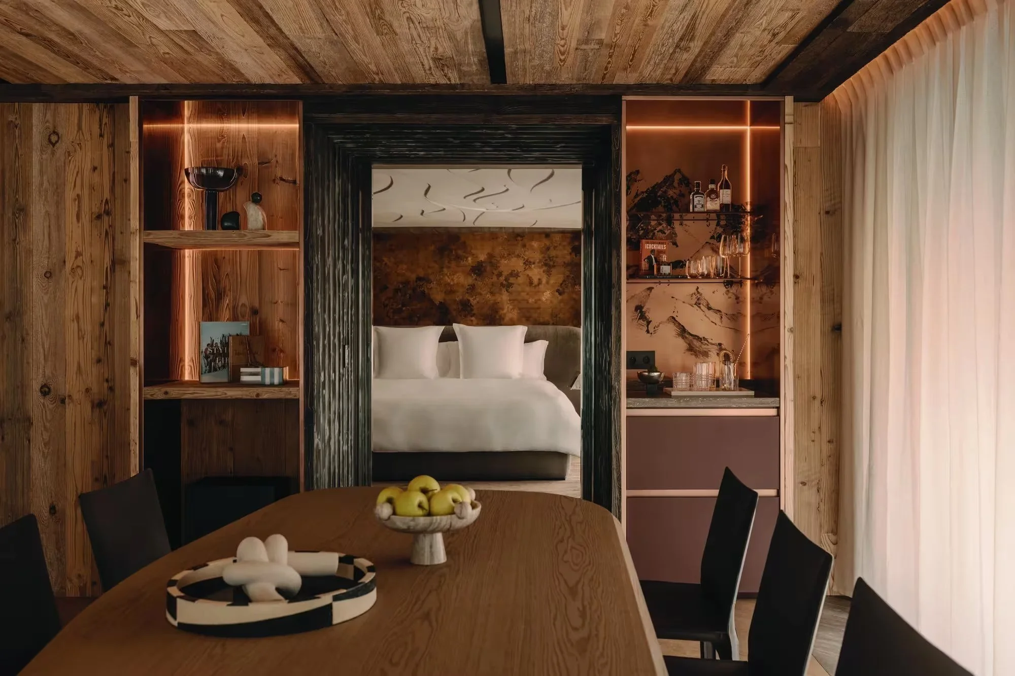Signature Suite living room with timber walls and open bedroom at Rosewood Courchevel Le Jardin Alpin