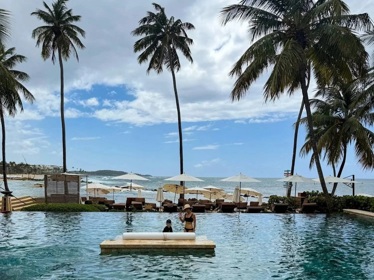 Author and her son in the oceanfront infinity pool at Dorado Beach, a Ritz-Carlton Reserve in Puerto Rico with palm trees in the background.