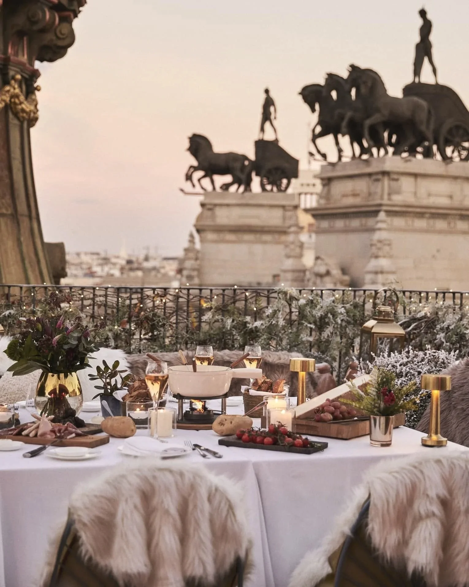 Winter table set for fondue on the rooftop terrace at Four Seasons Hotel Madrid, with the bronze chariot sculptures of Banco de Bilbao behind