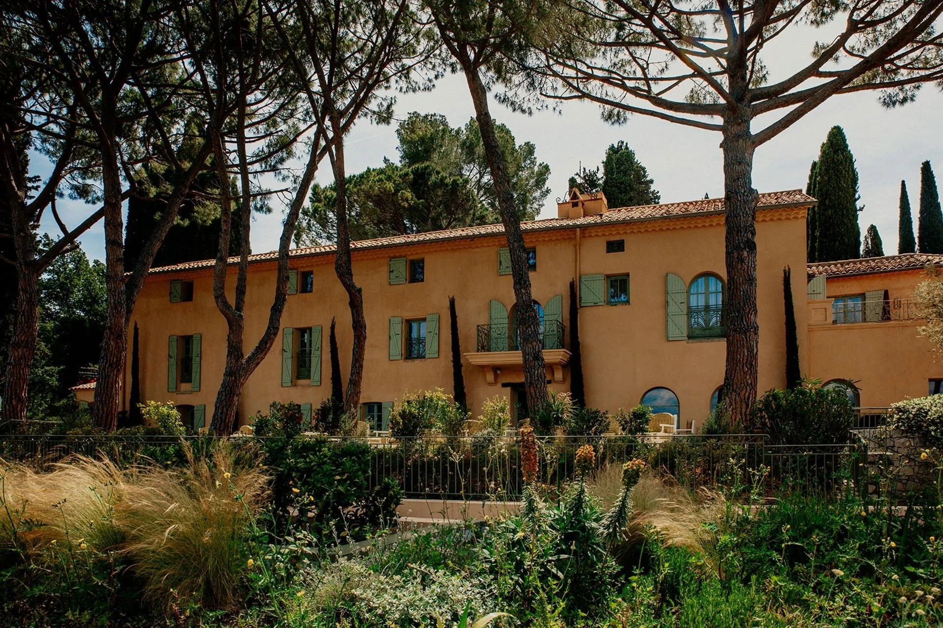 Traditional terracotta mansion exterior of Le Mas Candille surrounded by tall pine trees and lush gardens in Mougins.