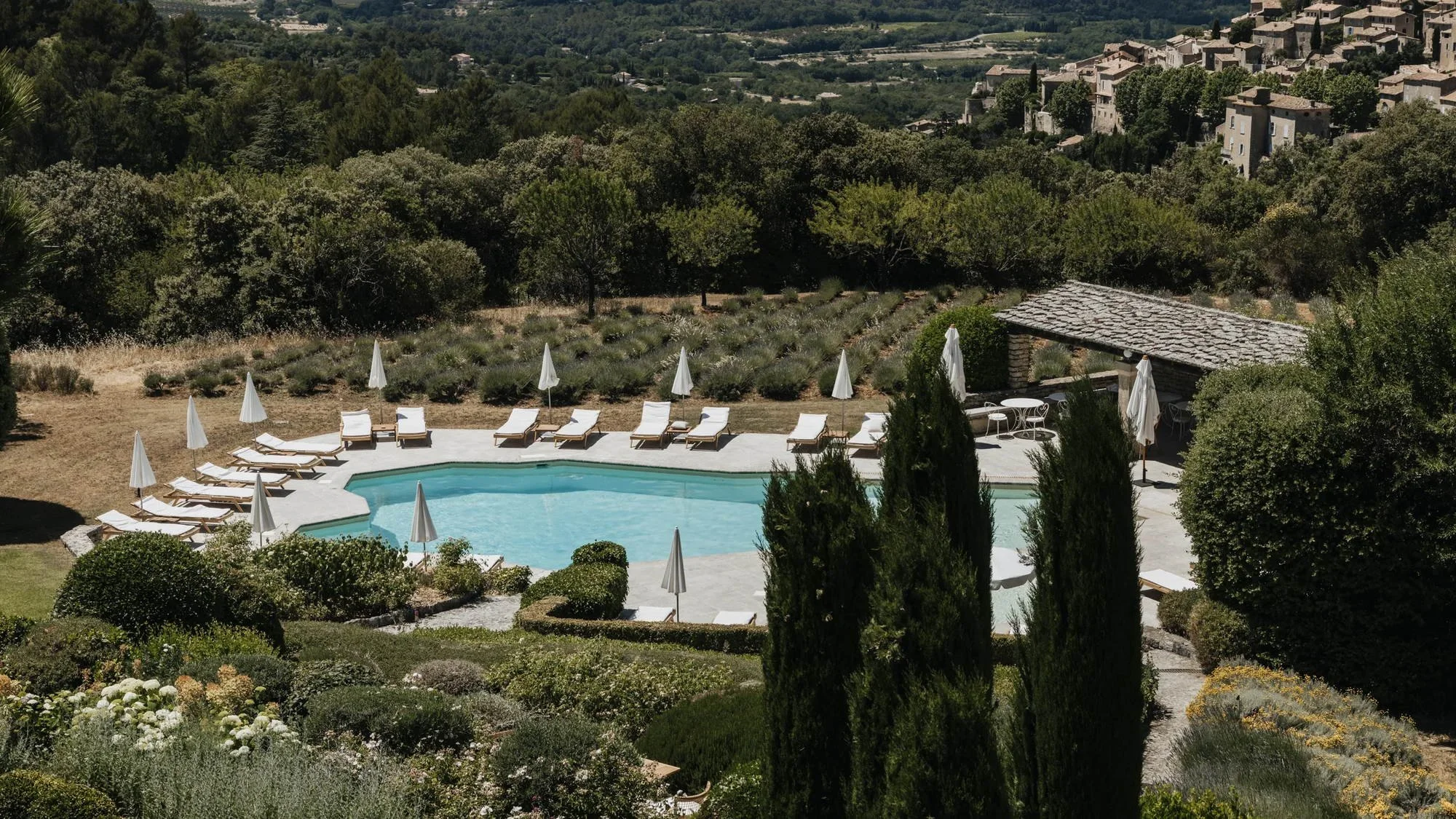 Main outdoor pool at Capelongue in Bonnieux with loungers, lavender and a hilltop village across the Luberon valley.