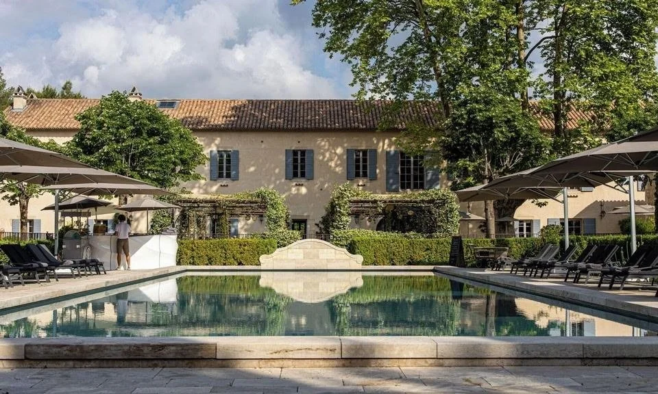 Outdoor pool at Domaine de Manville reflecting the stone facade and blue shutters under plane trees.