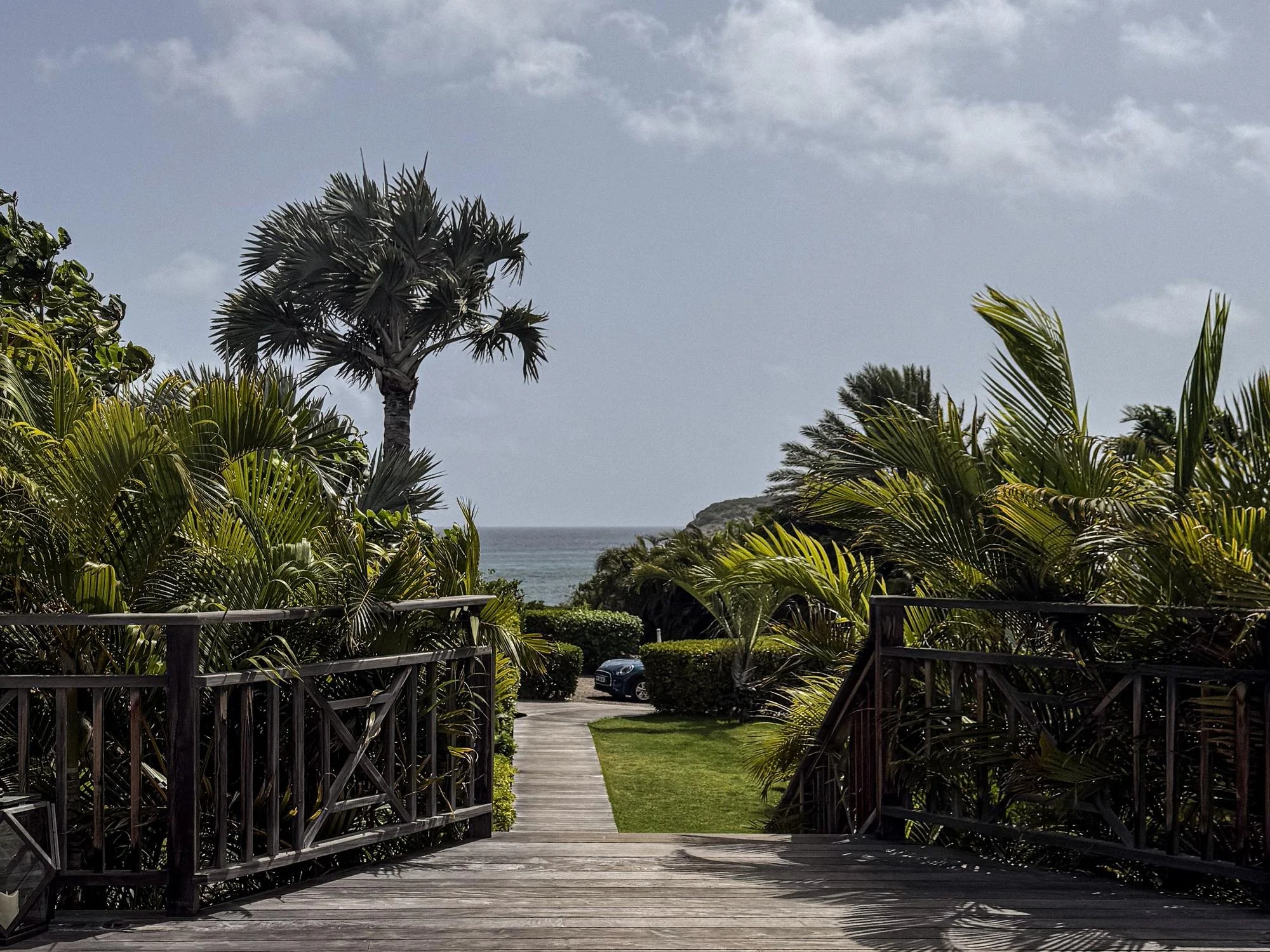 Tropical garden walkway winding through cottage accommodations at Rosewood Le Guanahani with a Mini Cooper parked nearby.