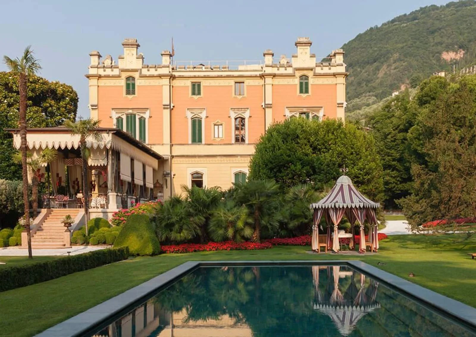 Grand Hotel a Villa Feltrinelli on Lake Garda, a pink neo-Gothic villa behind a manicured lawn with a striped garden pavilion and a reflecting pool.