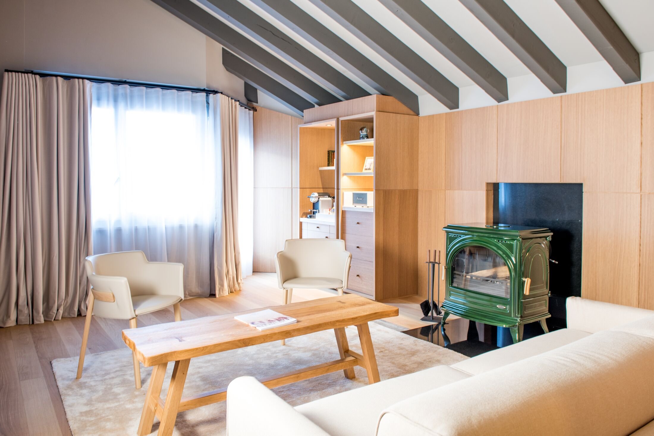 Cozy Attic Suite living room with exposed wood ceiling beams and green tiled stove at Schweizerhof Zermatt