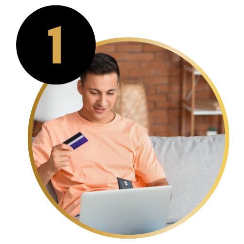 A young man sitting on a sofa, holding a credit card, shopping online on his laptop.