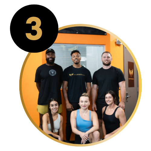 Group of six young adults in a fitness studio, three standing in the back and three sitting in front, smiling and wearing workout clothes.