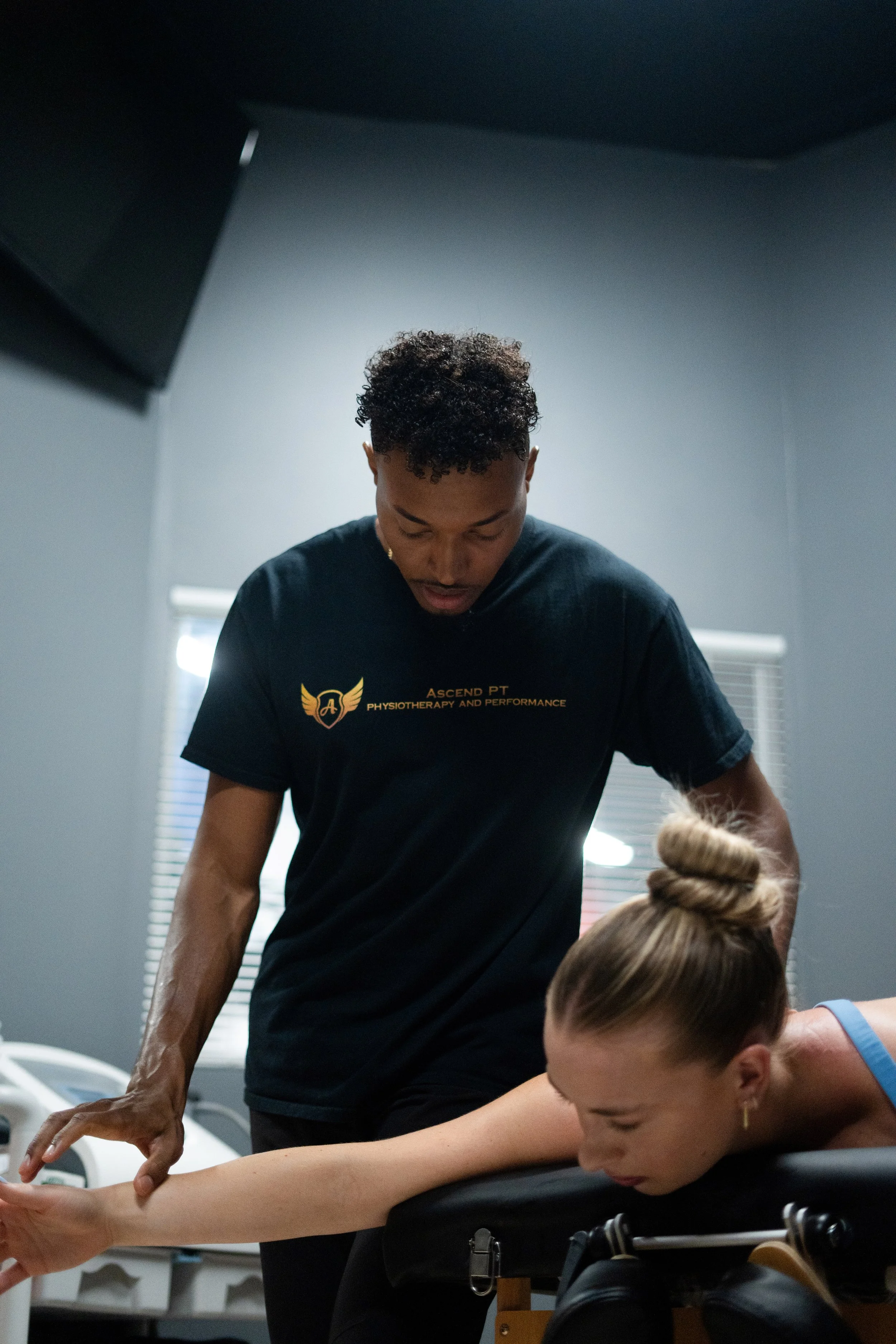A physiotherapist assists a woman with a stretching exercise on a treatment table in a therapy room.