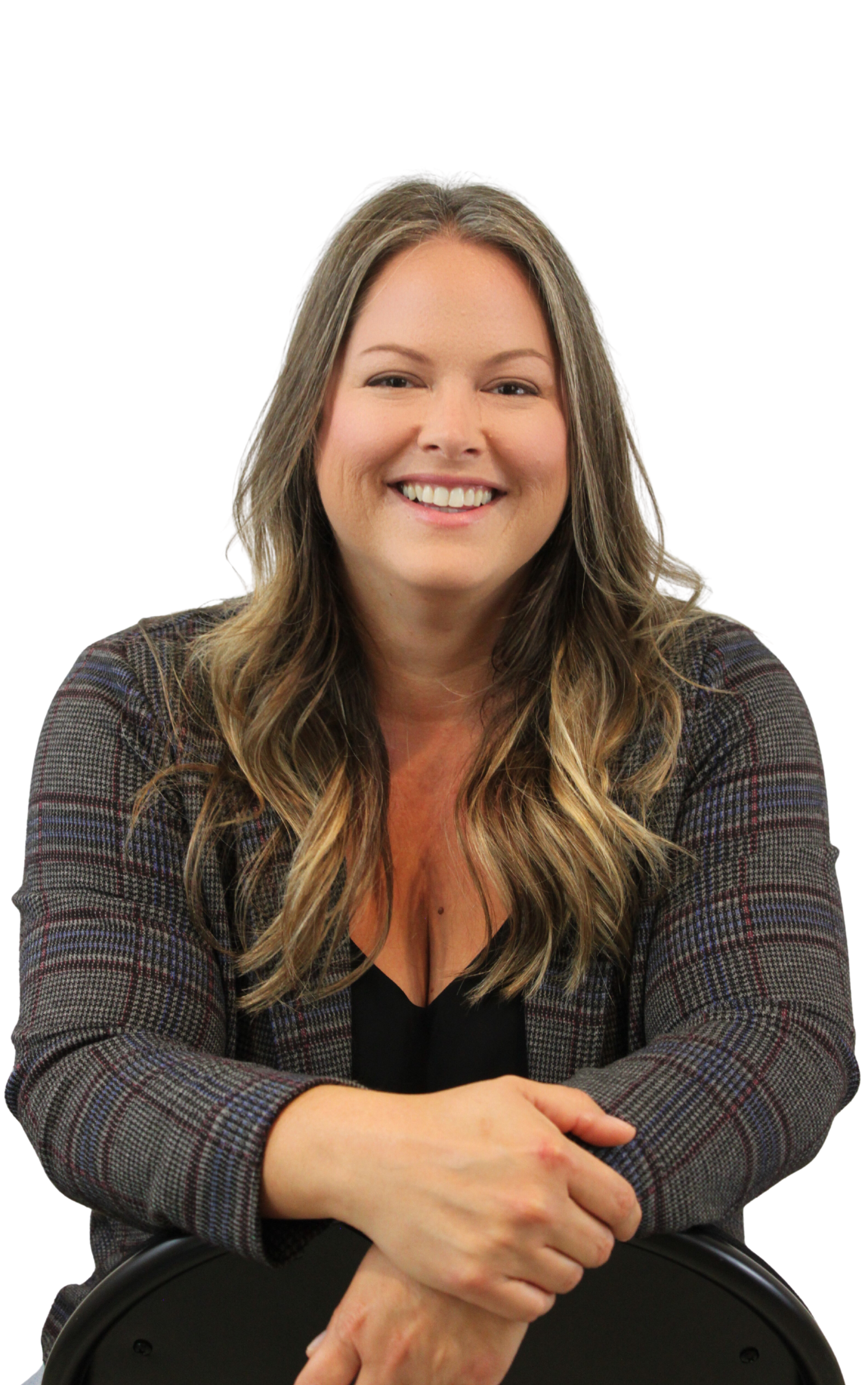 Smiling woman with long wavy hair sitting with folded arms, wearing a plaid blazer over a black top, seated at a table.