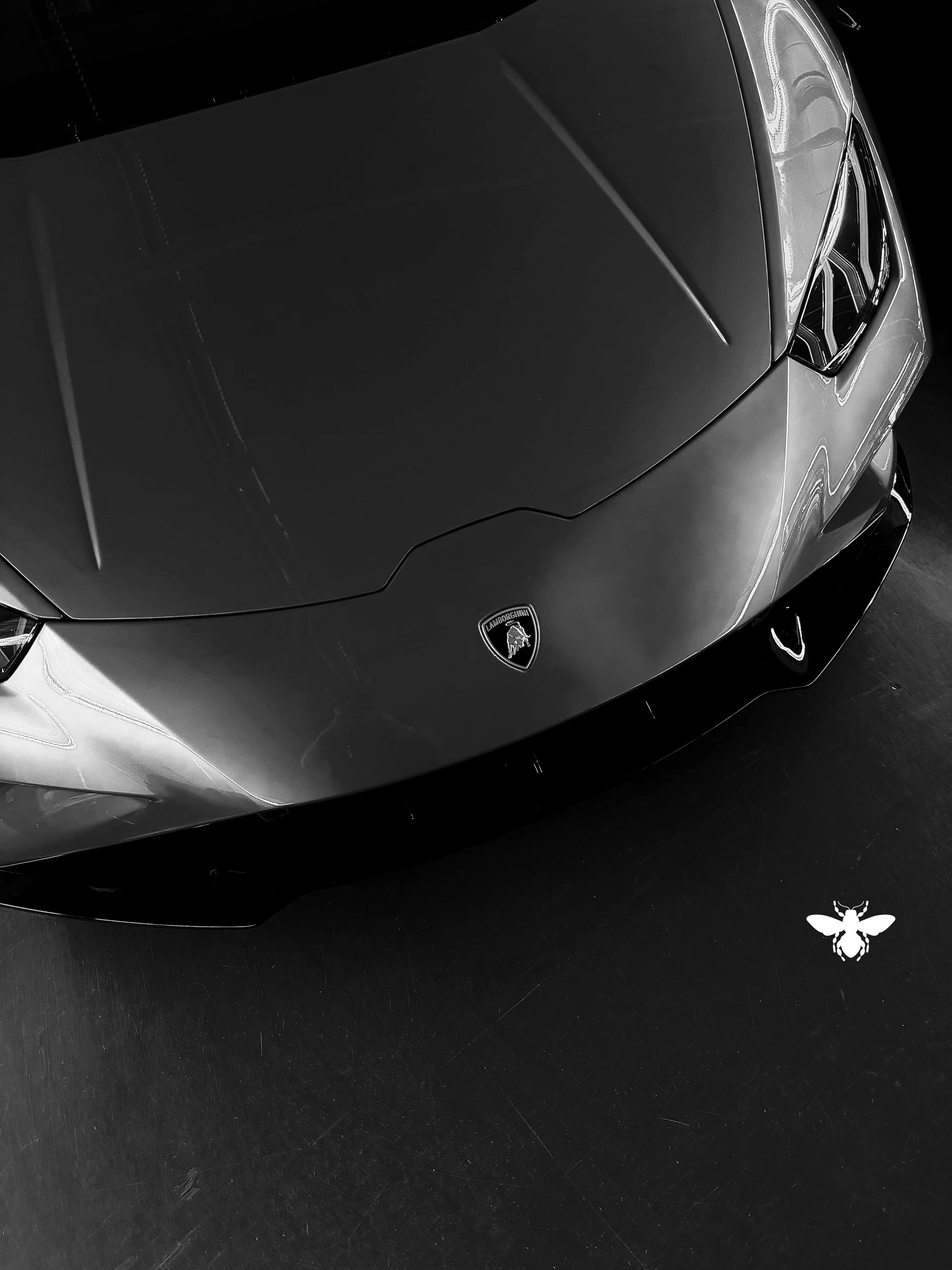 Black and white photo of a Lamborghini sports car viewed from above, showing the front of the car with the Lamborghini emblem visible.