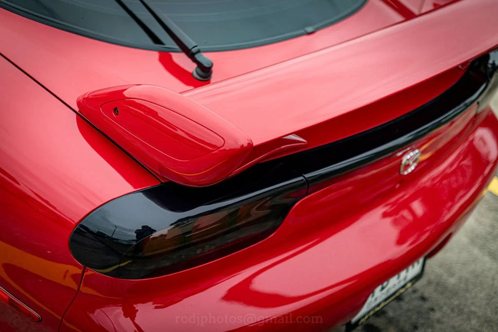 Close-up of the rear end of a red sports car, highlighting the taillights and a black spoiler.