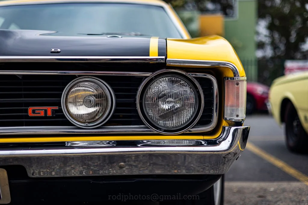 Close-up of the front end of a classic yellow and black Ford GT car, showing dual round headlights and grille.