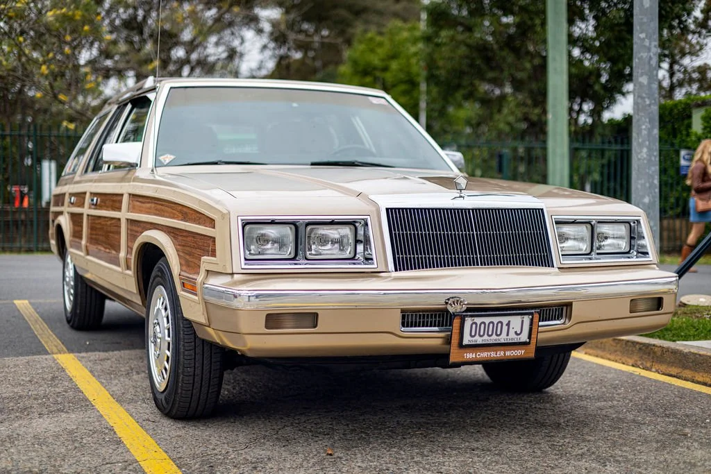 A beige 1994 Chrysler Woods station wagon parked in a parking lot with a license plate reading 00001 J.