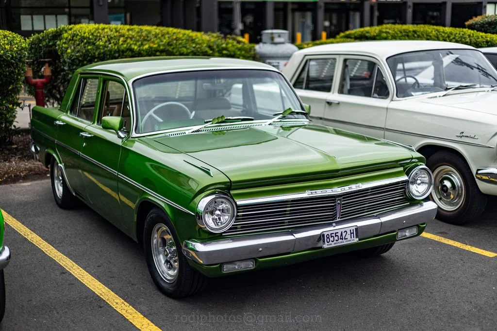 A vintage green Dodge car parked in a parking lot next to a beige classic car.