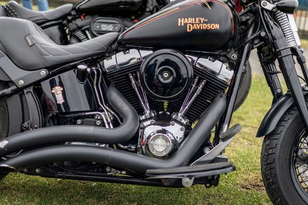 Close-up of a black Harley-Davidson motorcycle with chrome engine parts and black exhaust pipes, parked on grass.