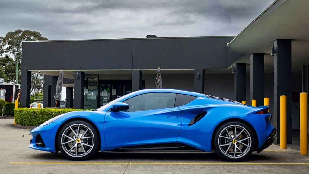A blue sports car parked in front of a modern building with yellow bollards.