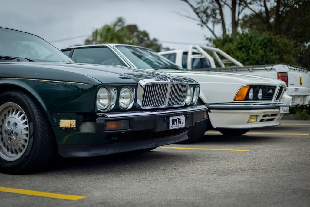 Several vintage cars parked in a lot with trees in the background.
