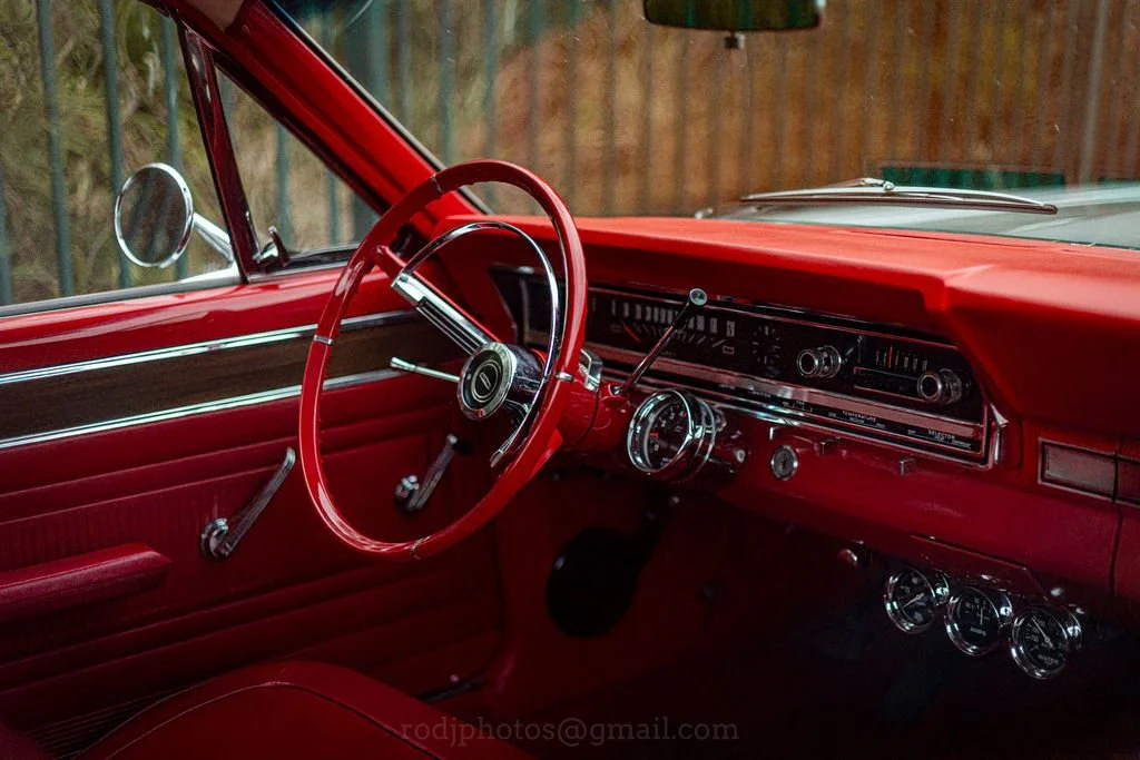 Interior of a vintage red car with a red steering wheel, dashboard, and leather seats, featuring classic gauges and controls.