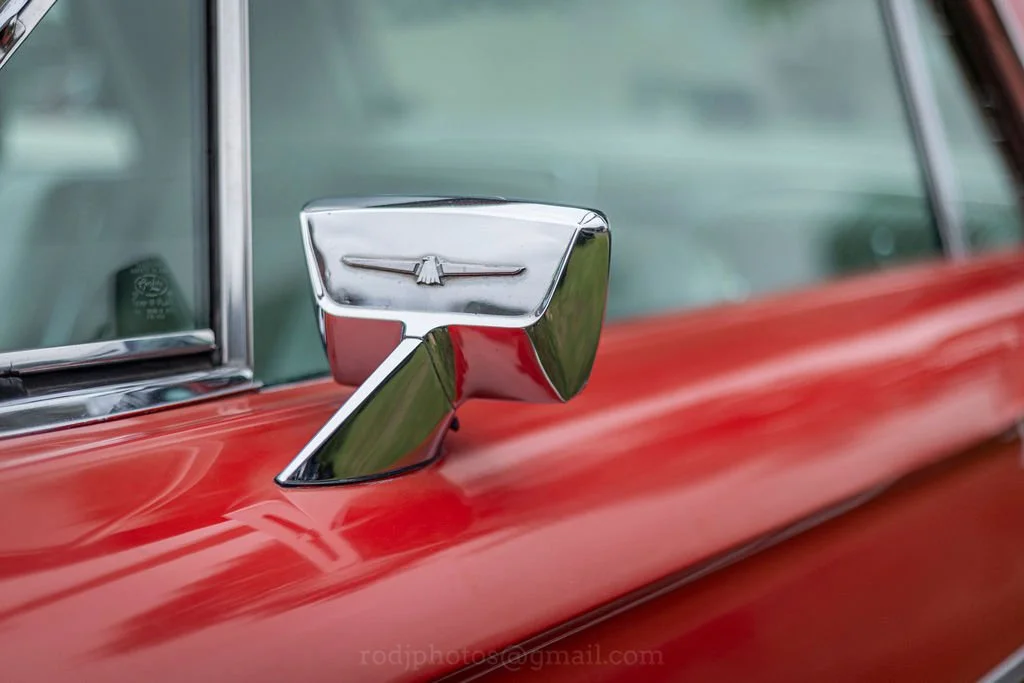 Close-up of a chrome rearview mirror on a vintage red car with a winged emblem.