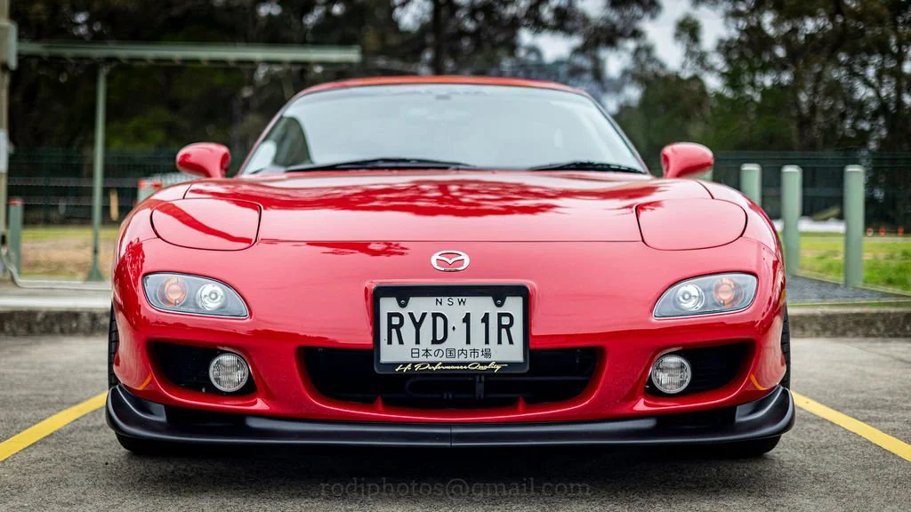 Front view of a red Mazda RX-7 sports car parked in a parking lot.