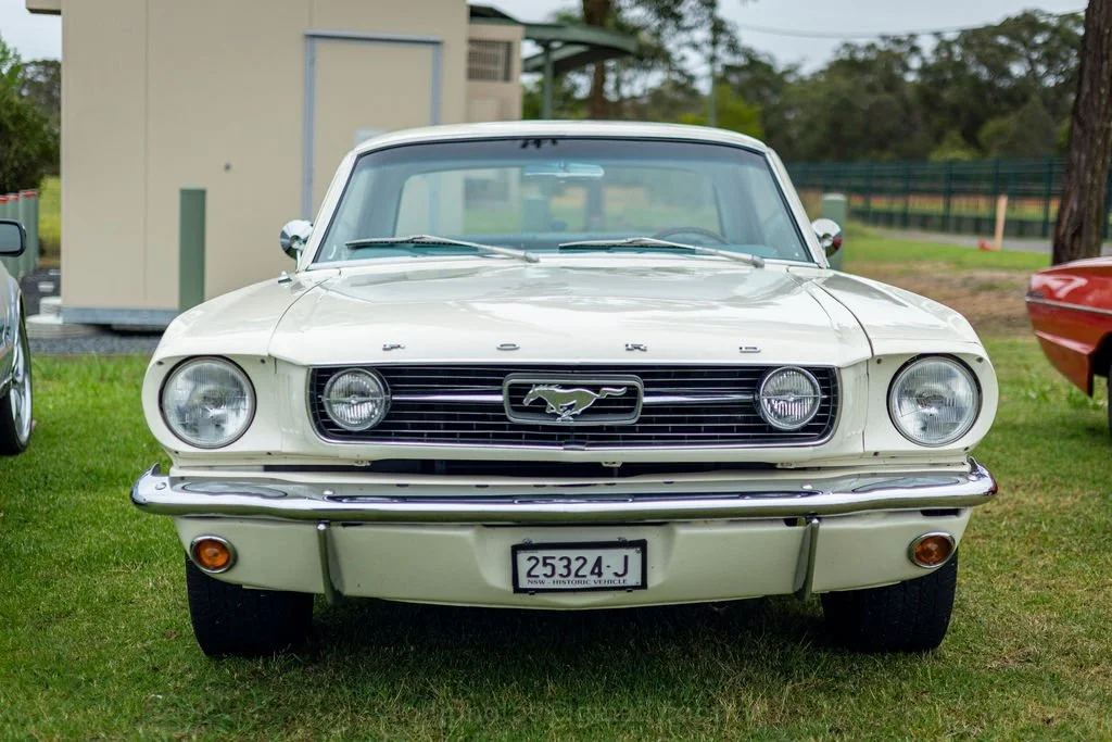 Front view of a classic white Ford Mustang car parked on grass.