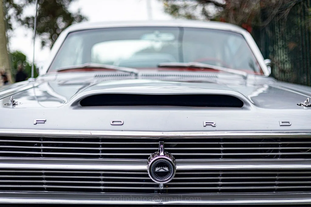 Front view of a classic silver Ford car, highlighting the grille with the Ford logo and the hood scoop.