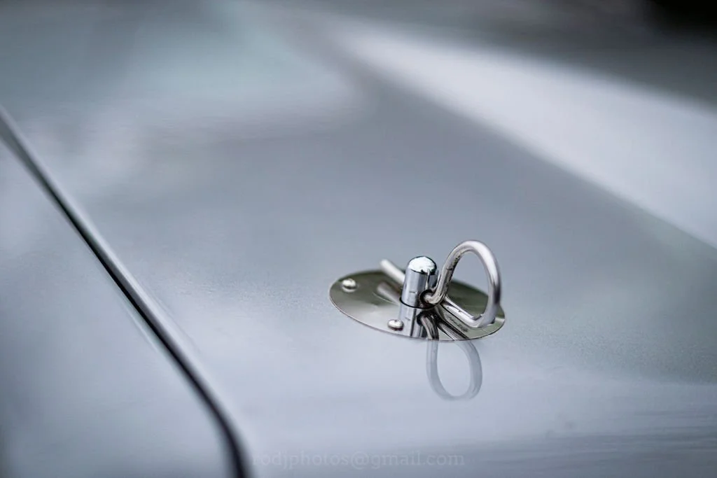 Close-up of a metallic latch on a gray vehicle hood.