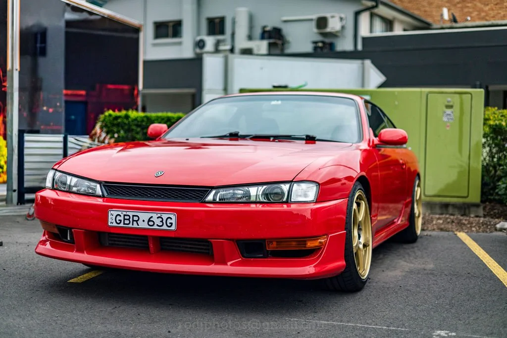 A red sports car with gold wheels parked in a parking lot.