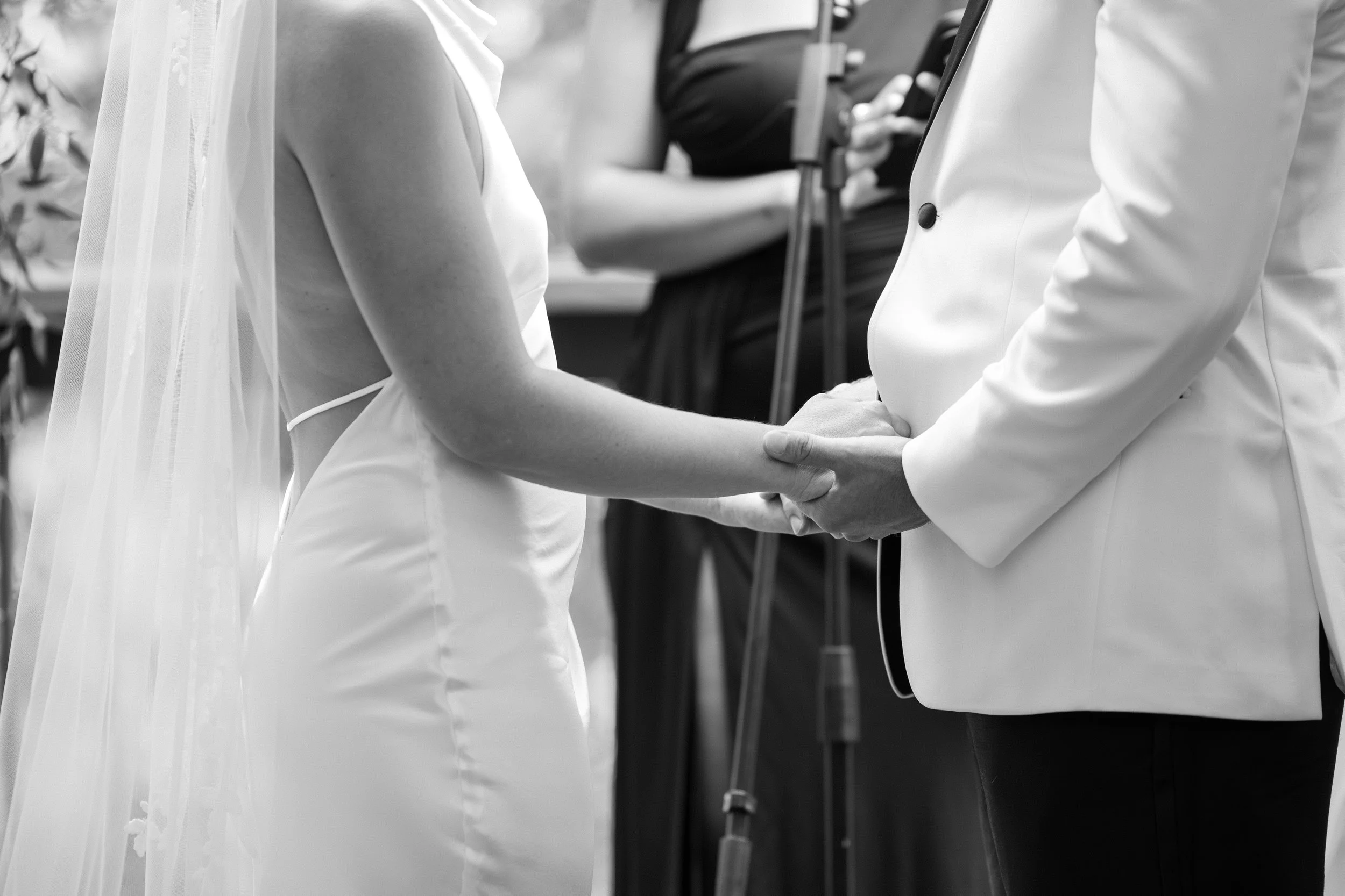 A bride and groom holding hands during their wedding ceremony, with wedding officiant in background.
