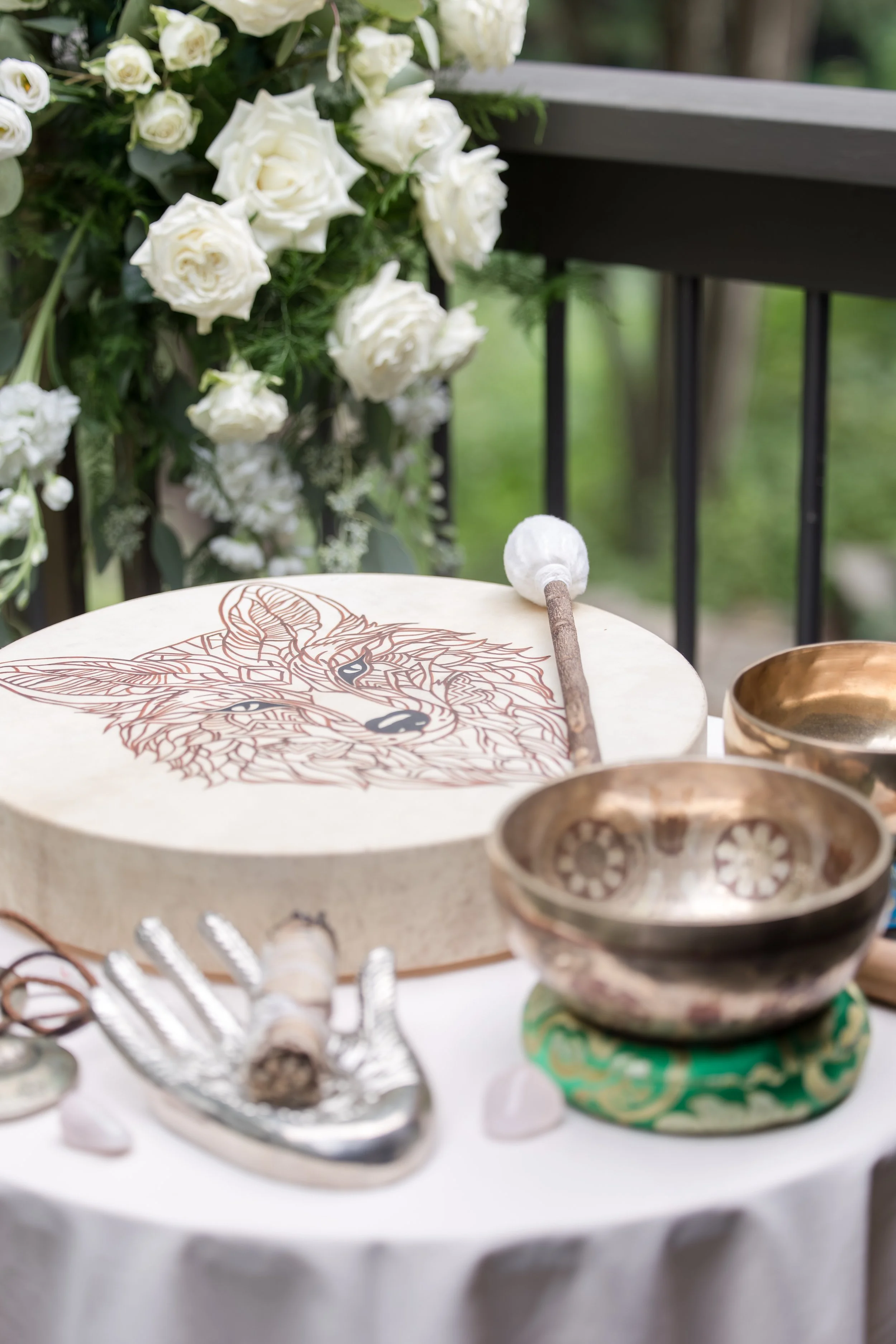 Decorative table with singing bowl, mallet, and dog artwork, with white roses in the background.