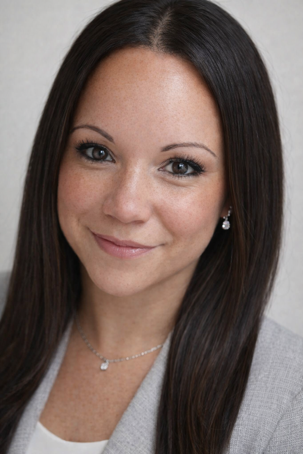 Close-up of a smiling woman with long dark hair, wearing pearl earrings and a matching necklace.