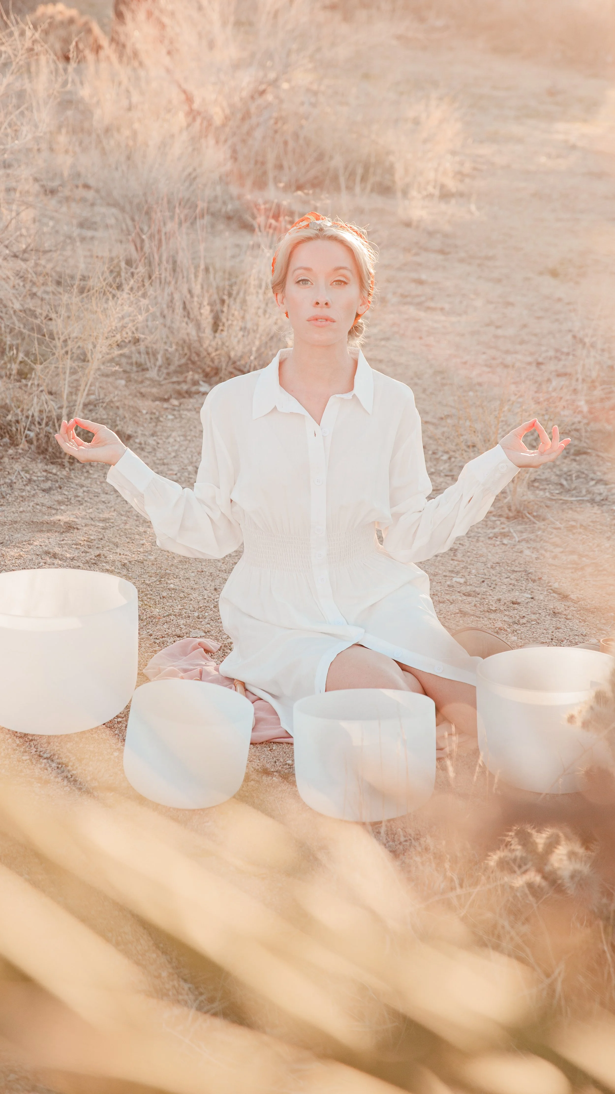 Person meditating outdoors with sound bowls in a desert setting.