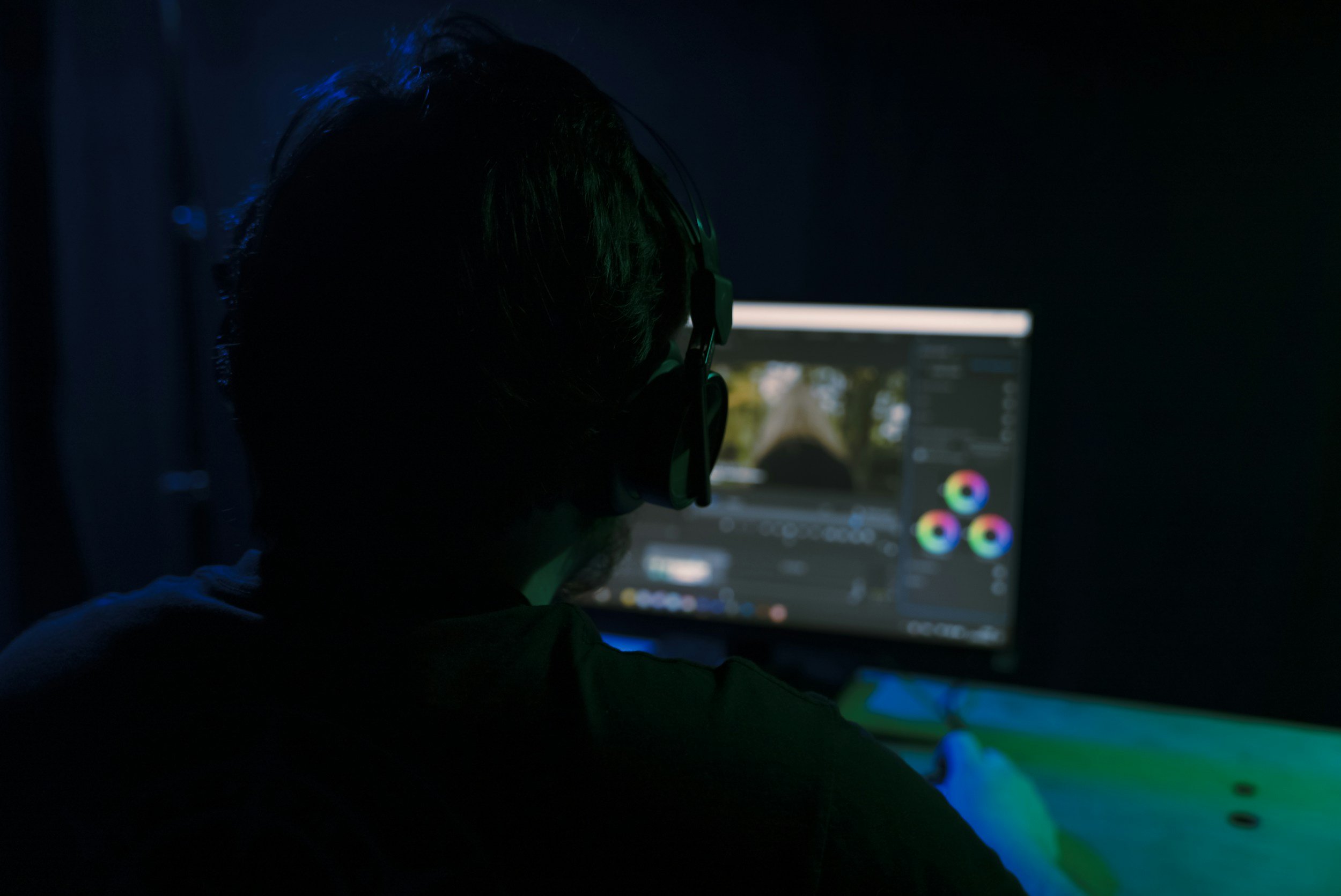 Person wearing headphones editing video on a computer in a dark room