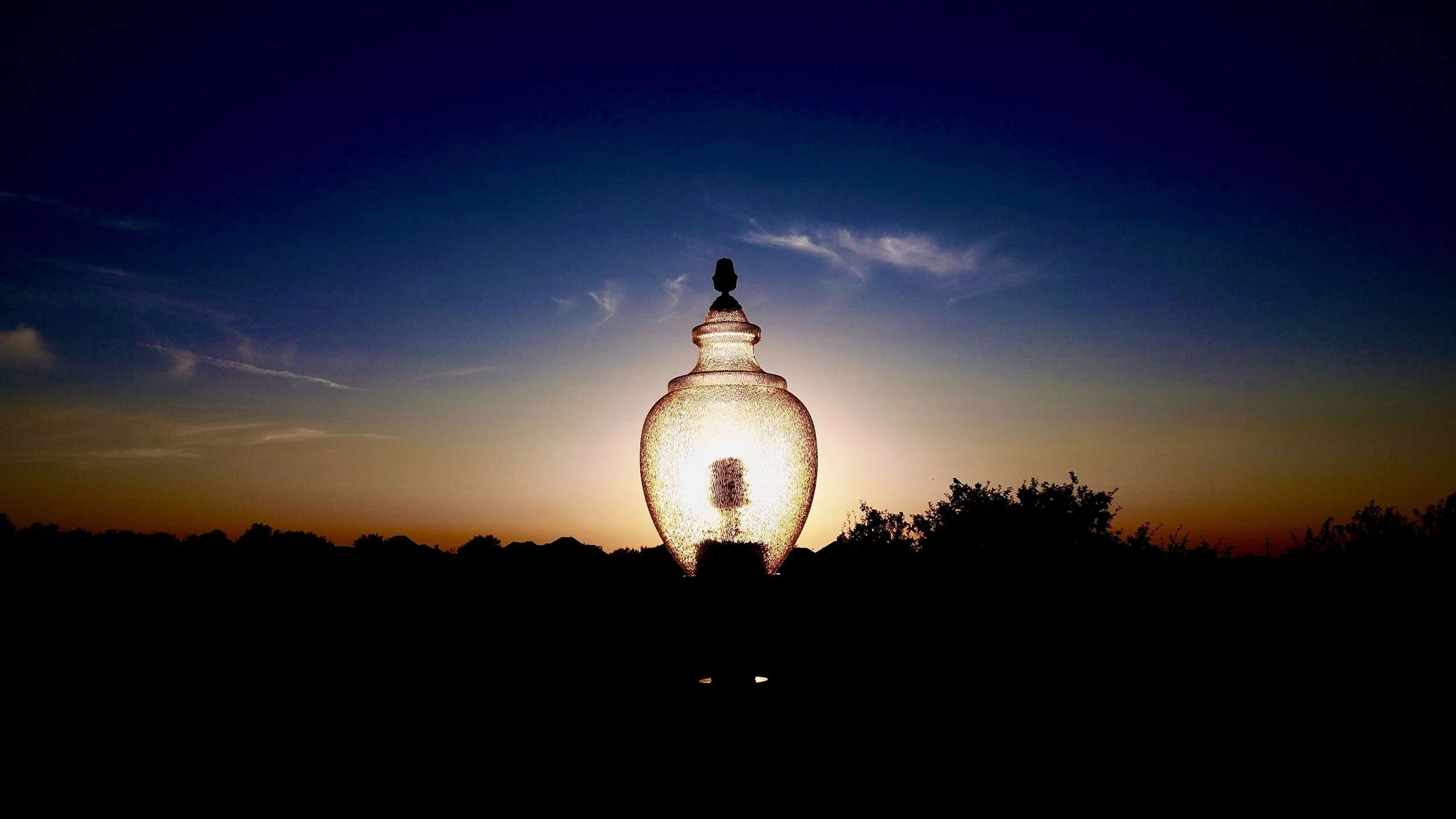 Silhouette of a decorative glass lamp against a sunset with blue and orange sky.