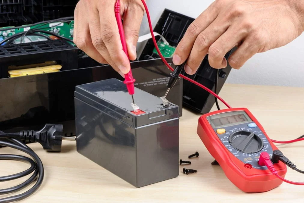 Person testing a rechargeable battery with a multimeter and a multimeter probes.