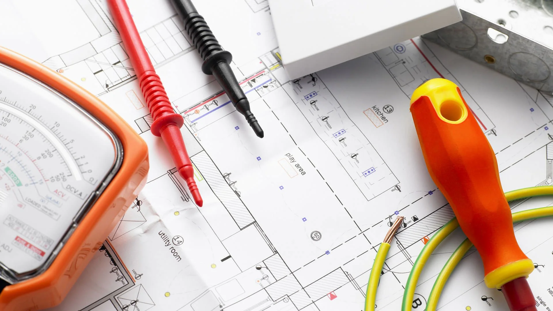 Construction electrical tools and a blueprint, including a multimeter, test probes, and a cordless electric screwdriver on an electrical plan.