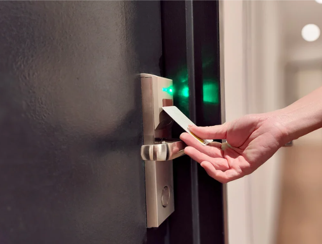 Hand holding a key card near an electronic door lock with a green indicator light.