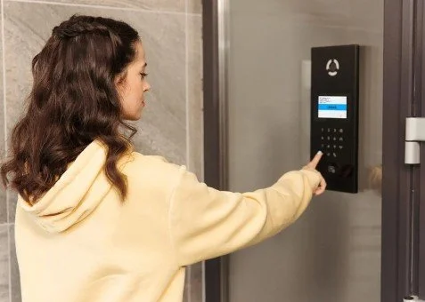 A woman in a yellow hoodie using a security keypad on an elevator door.