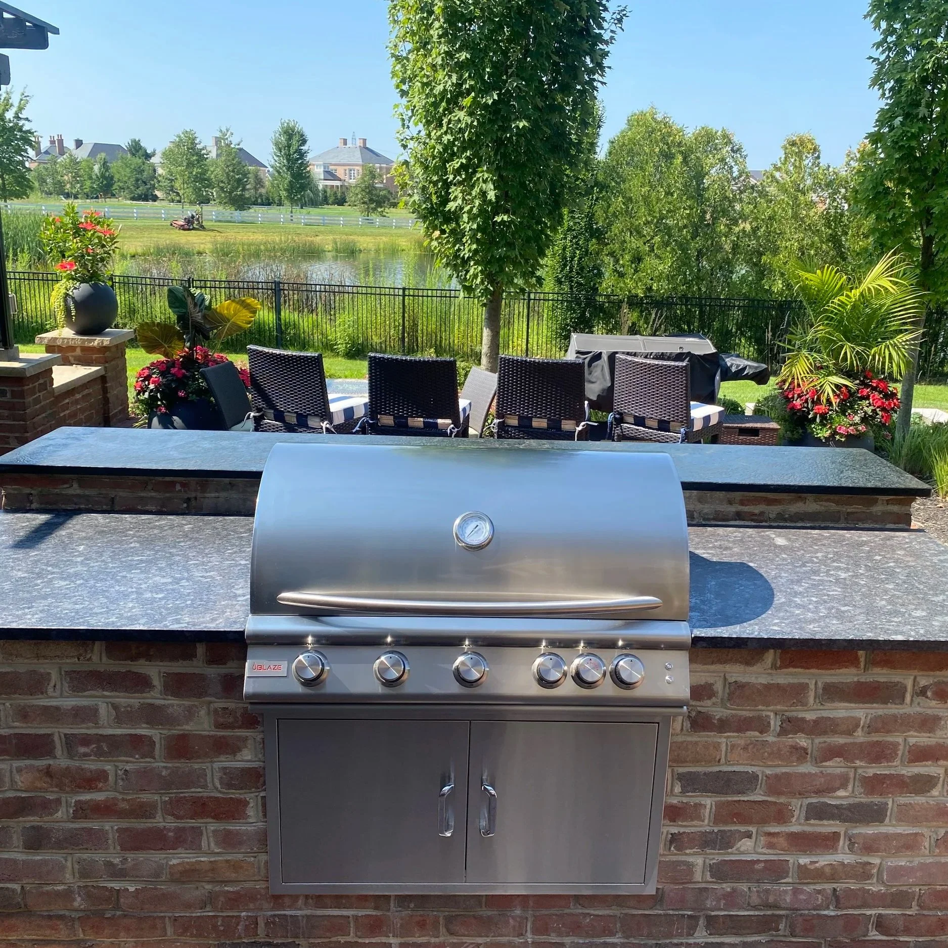 Stainless steel outdoor grill on brick patio in a backyard with garden, trees, and lake view. Blaze natural gas grill from BBQ guys. Granite countertops from Pro-Mo Granite. New Albany, Ohio 43054