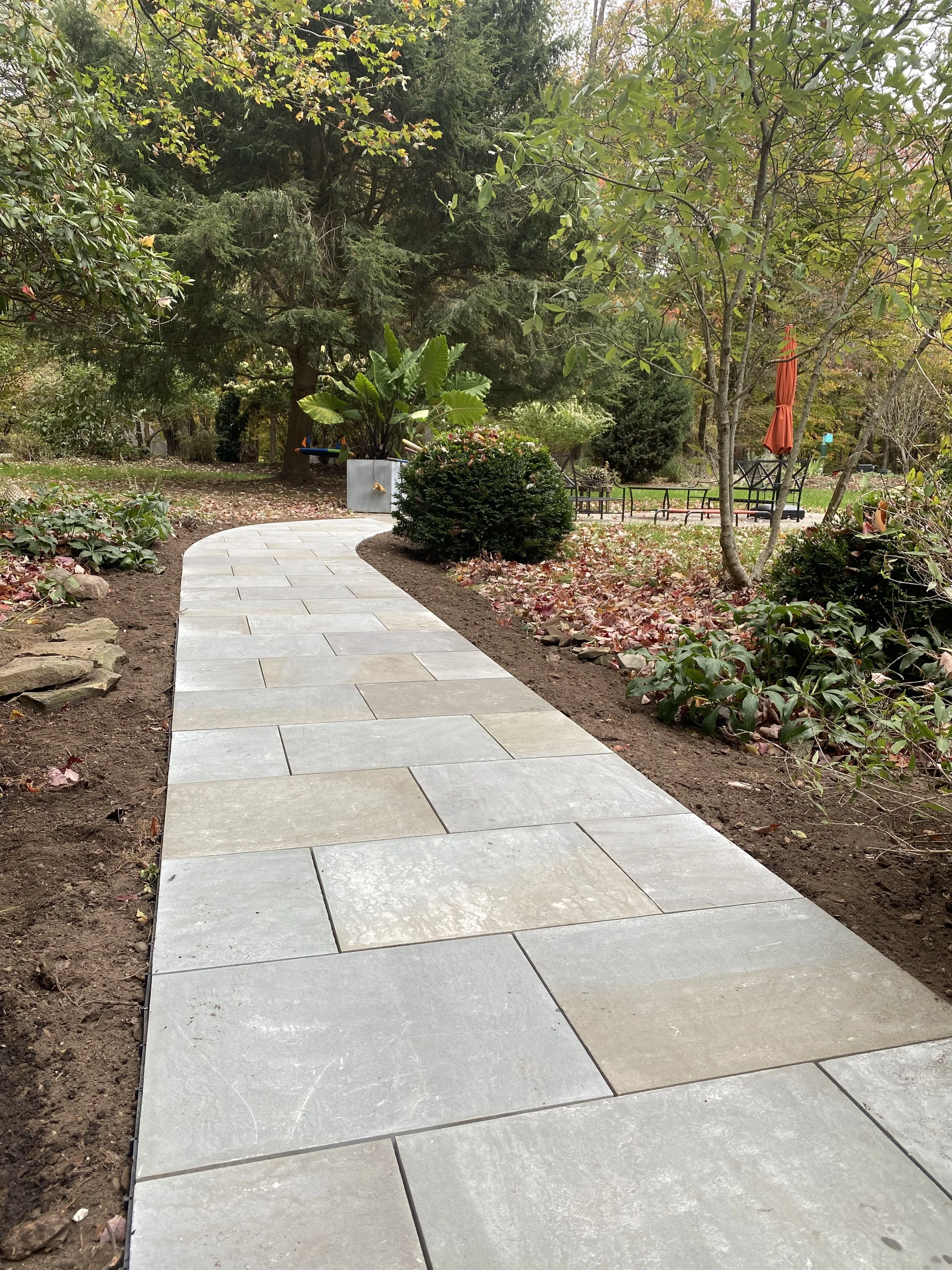 A curved Pennsylvania bluestone pathway in a garden with trees, shrubs, and garden furniture. Granville, Ohio