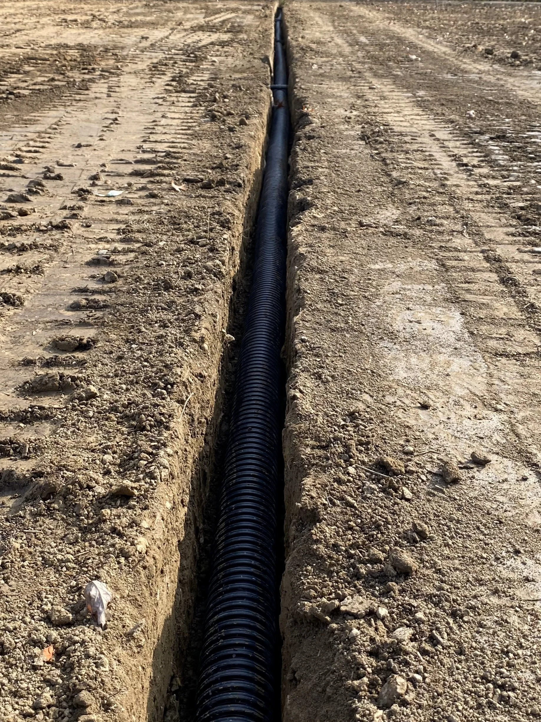 A long black corrugated pipe running through a dug trench in a dirt road or construction site. drainage excavation grading seeding sodding