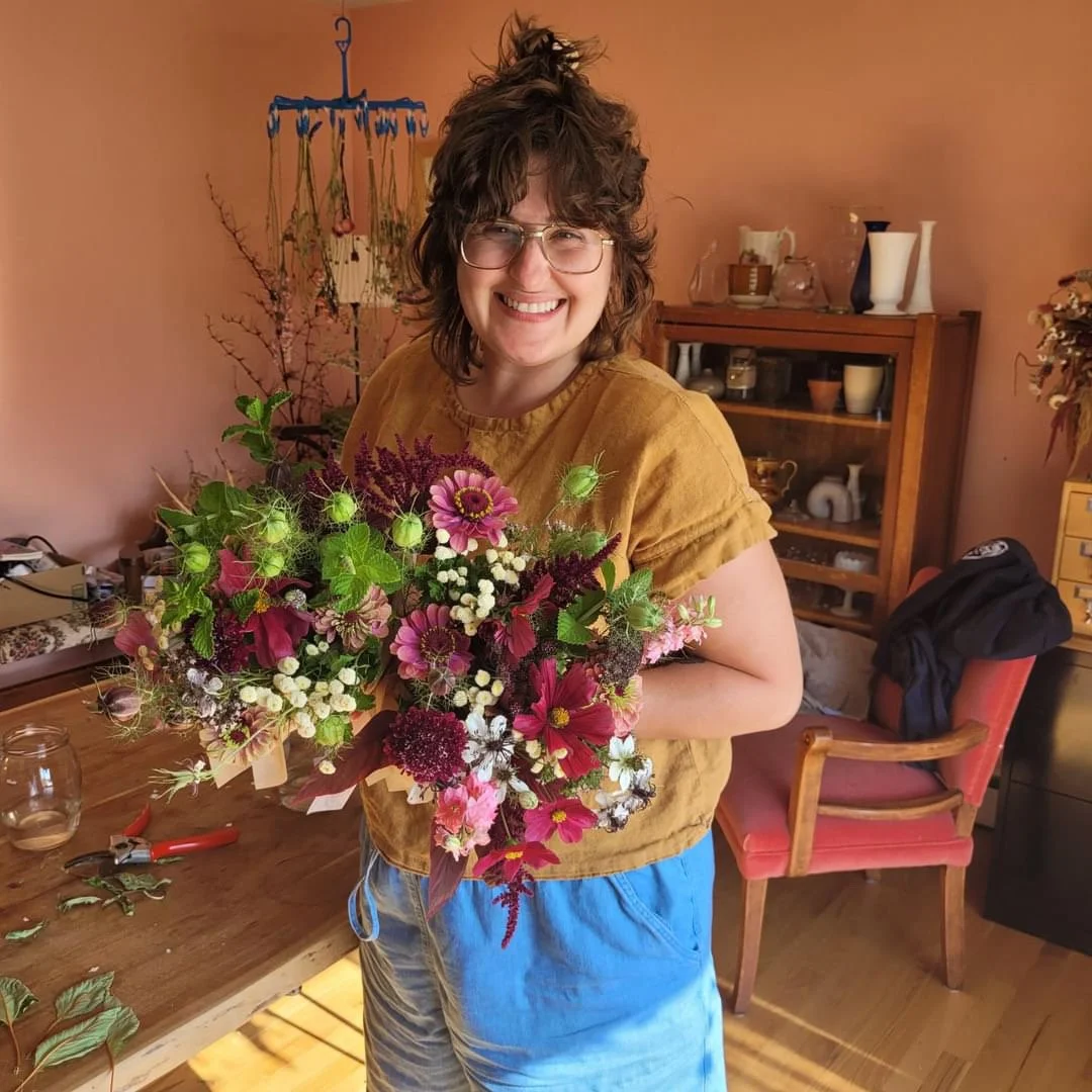 Personne souriante tenant des bouquets de fleurs colorées dans une pièce à l'intérieur.