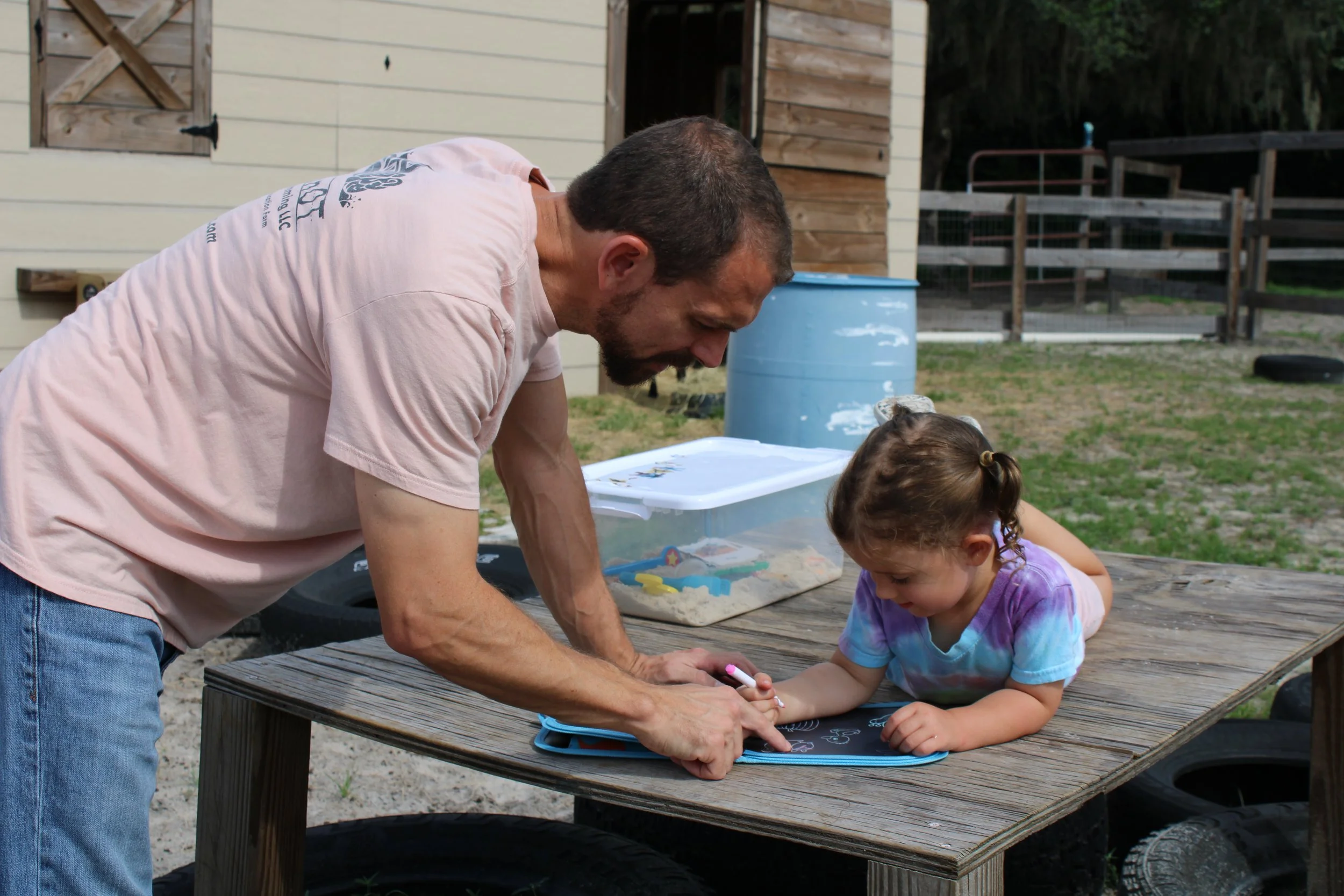 Child writing in goat enclosure with OT