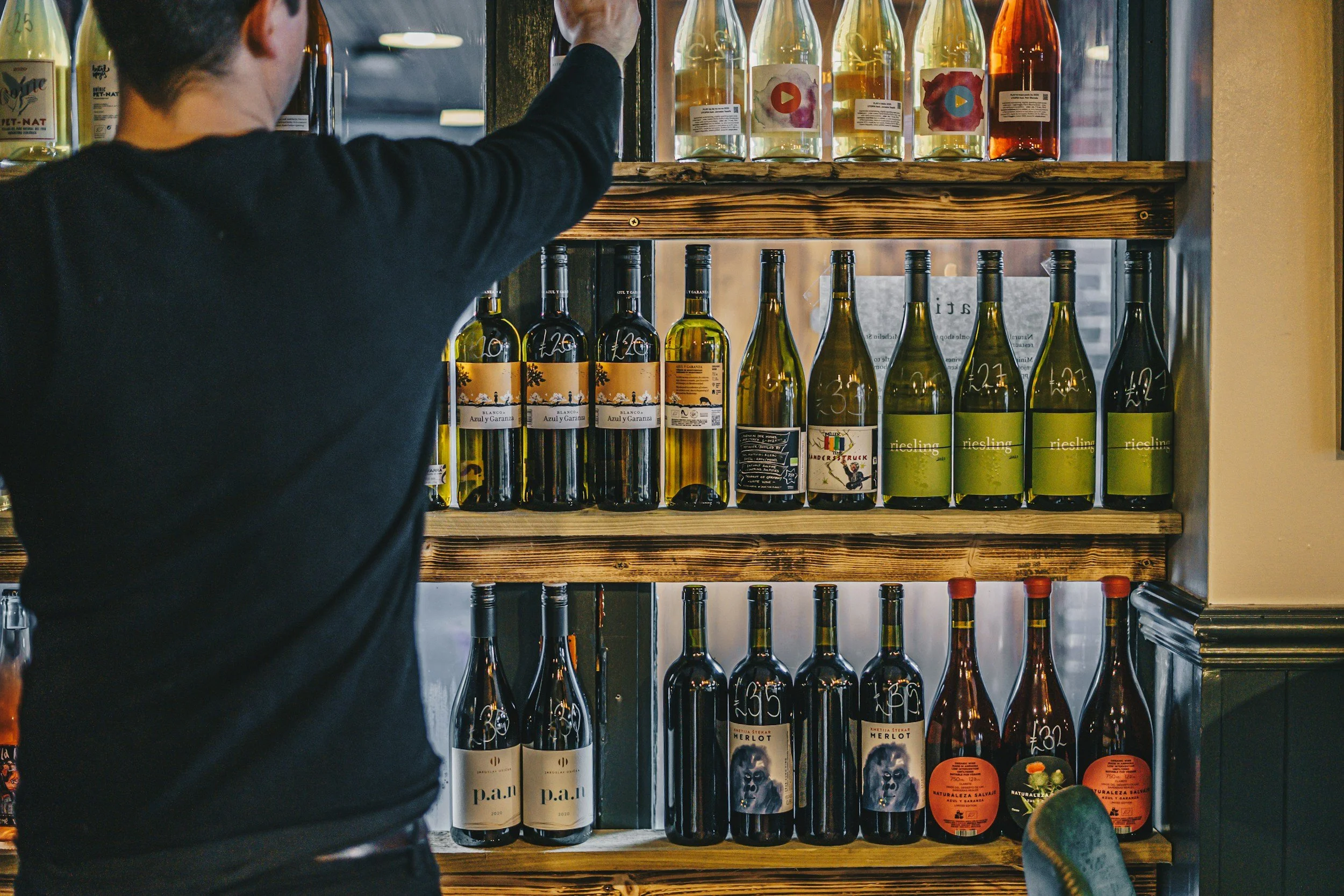 Person browsing and selecting wine bottles from a curated wine shop display during a wine shopping experience