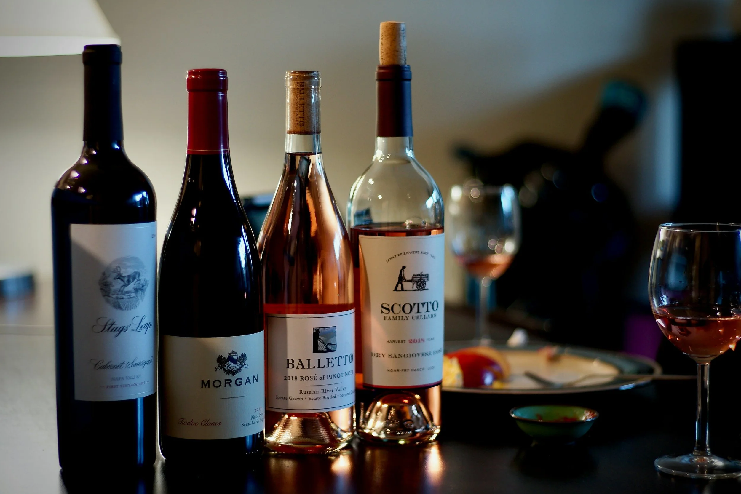 Red, rosé, and white wine bottles prepared for a home wine tasting with glasses and light appetizers.