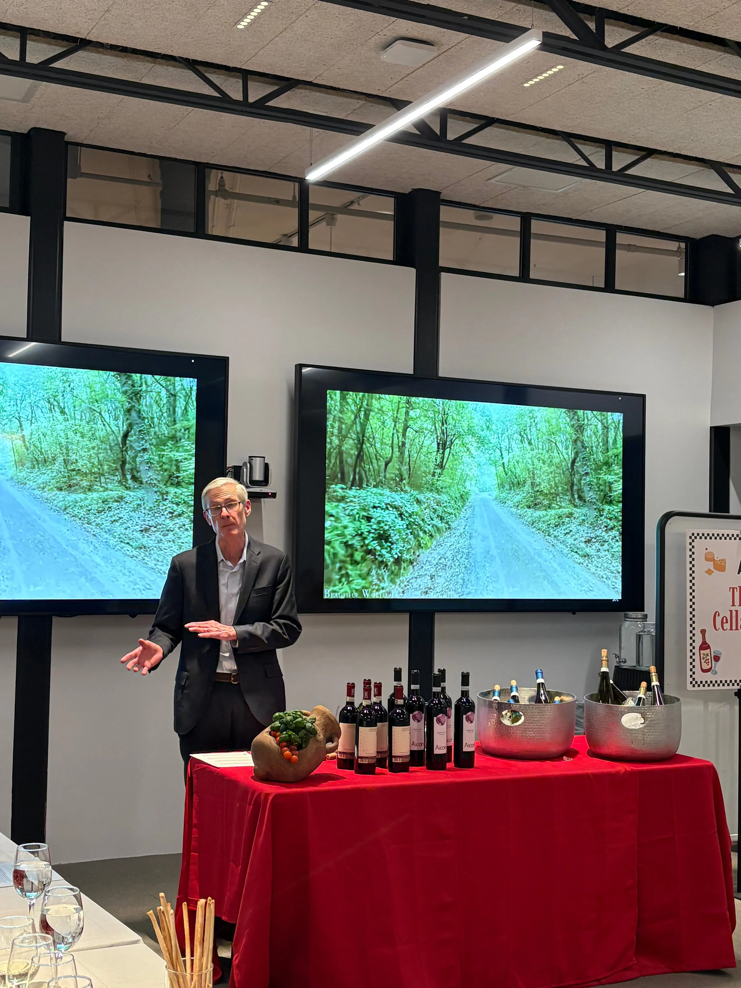 People gathered around a wooden table, pouring and holding glasses of wine in a social setting.