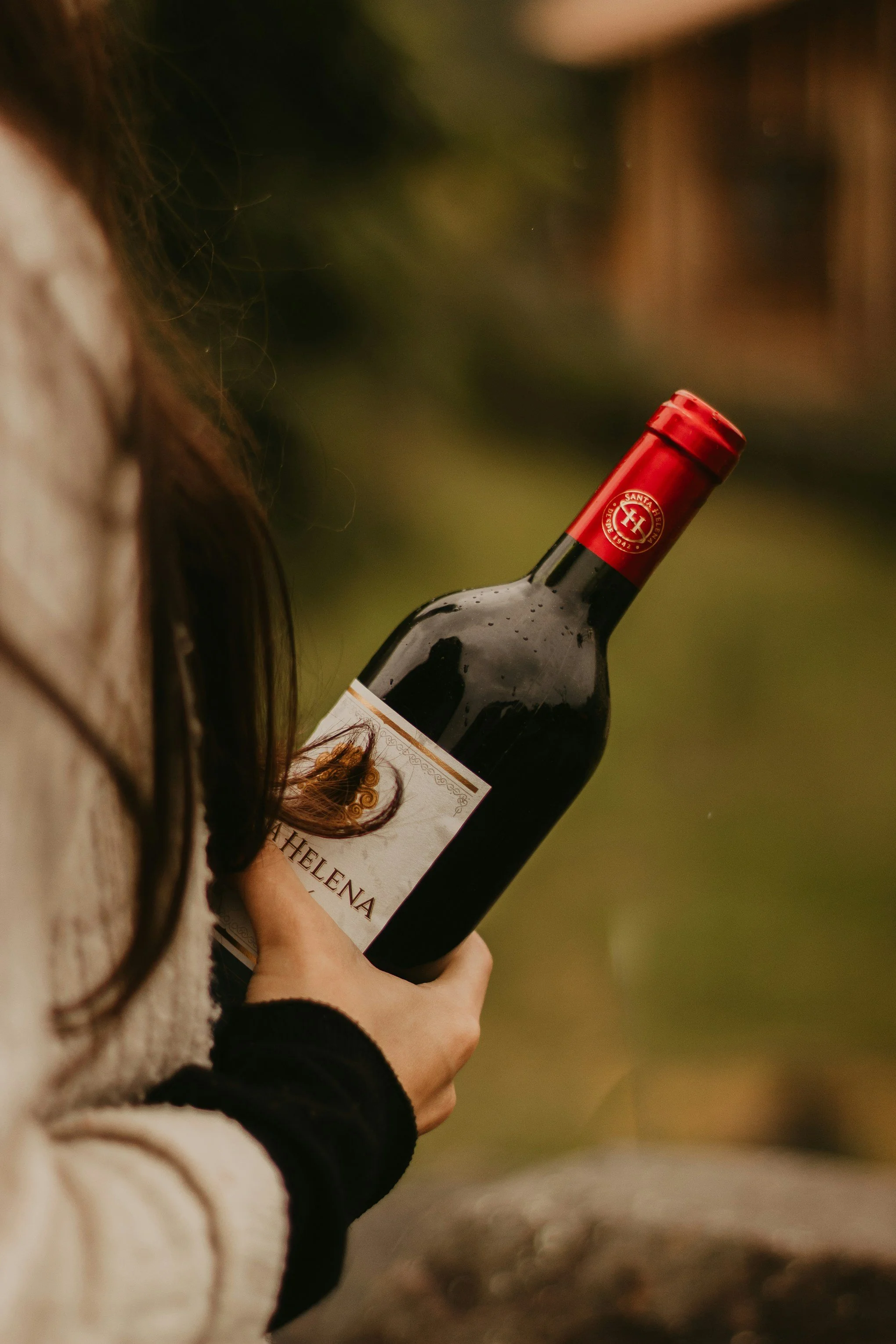 Person holding a bottle of red wine outdoors during a wine tasting and wine appreciation experience