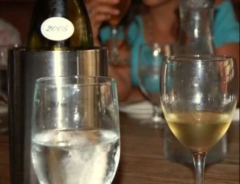 Glass of white wine on a restaurant table with a bottle in a cooler, illustrating improper wine serving temperature